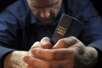 A Man praying holding a Holy Bible