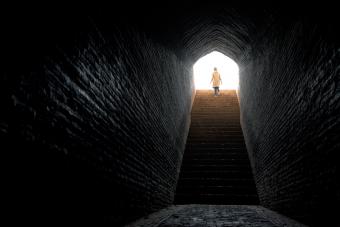 Woman timidly stepping into bright light coming out from dark tunnel