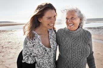 adult daughter laughing and walking on beach with elderly mother