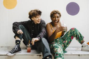 Cheerful friends sitting with drinks on retaining wall