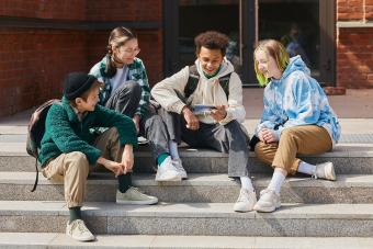 Group of teenage students sitting outside school buildings